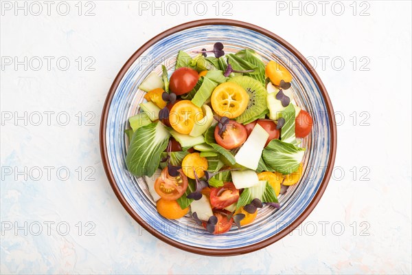 Vegetarian salad of pac choi cabbage, kiwi, tomatoes, kumquat, microgreen sprouts on a white