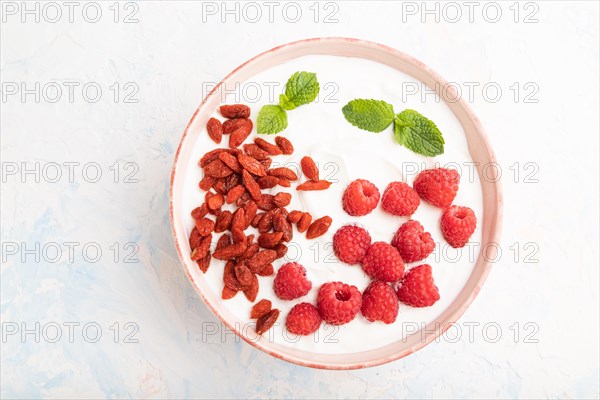 Yogurt with raspberry and goji berries in ceramic bowl on white concrete background. top view, flat