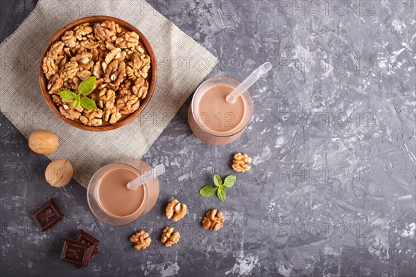 Organic non dairy walnut chocolate milk in glass and wooden plate with walnuts on a black concrete