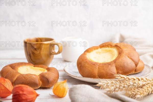 Sour cream bun with cup of coffee on a white wooden and concrete background and linen textile. Side