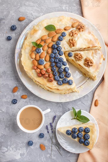 Homemade layered Napoleon cake with milk cream. Decorated with blueberry, almonds, walnuts,
