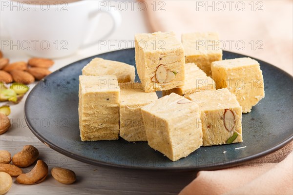 Traditional indian candy soan papdi in a blue ceramic plate with almond, pistache, cashew and a cup
