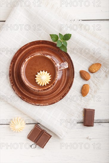 Cup of hot chocolate and pieces of milk chocolate with almonds on a white wooden background with