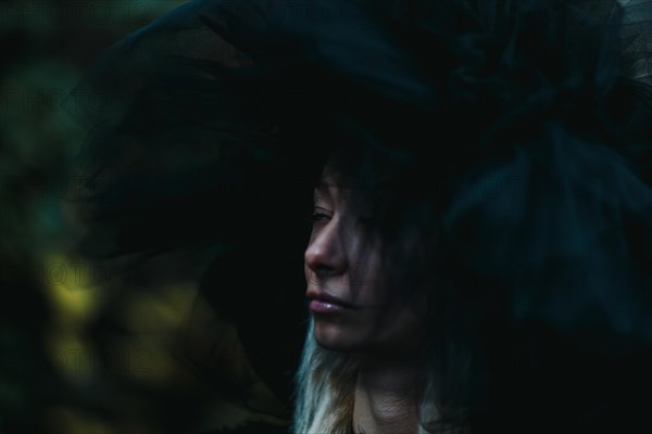 A white thin caucasian blonde woman in shadows wears a large hat, creating a moody and