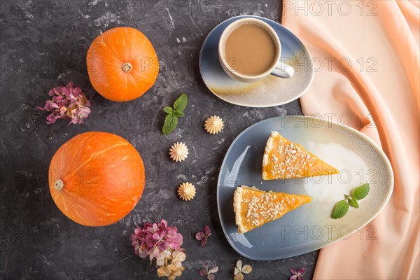 Two pieces of traditional american pumpkin pie with cup of coffee and pumpkins on a black concrete