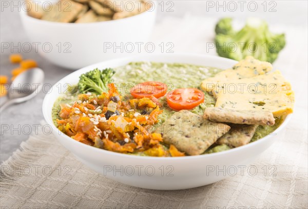 Green broccoli cream soup with crackers and cheese in white bowl on a gray concrete background and