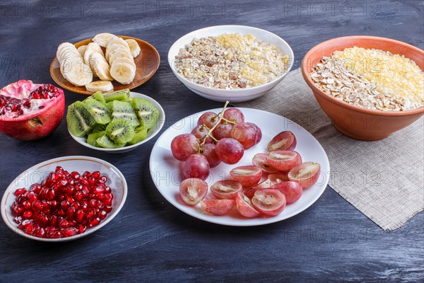 A set of plates with muesli, grapes, kiwi, pomegranate, banana on a black wooden background. close