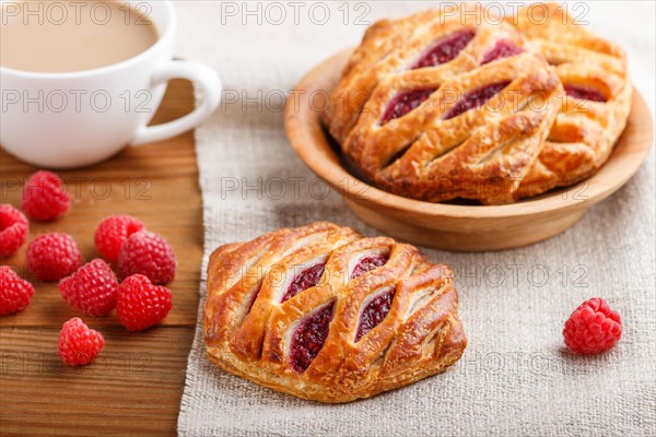 Puff pastry buns with strawberry jam on wooden background with linen textile and a cup of coffee.