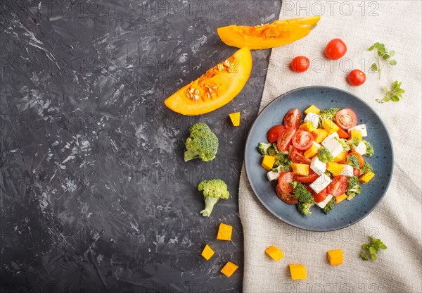 Vegetarian salad with broccoli, tomatoes, feta cheese, and pumpkin on a blue ceramic plate on a
