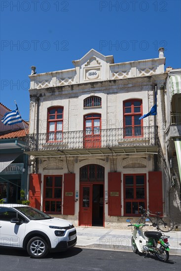 Historic neoclassical building with striking red windows and parked scooter, Museum of Silk Art,