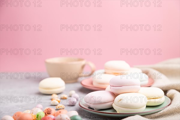 Colored zephyr or marshmallow with cup of coffee and dragees on a gray and pink background and