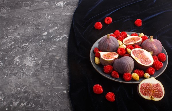 Fresh figs, strawberries and raspberries on blue ceramic plate on black concrete background and