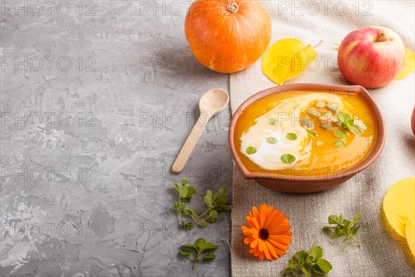 Traditional pumpkin cream soup with seeds in clay bowl on a gray concrete background with linen