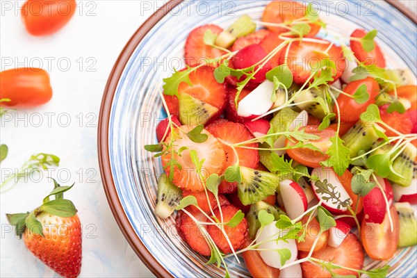 Vegetarian fruits and vegetables salad of strawberry, kiwi, tomatoes, microgreen sprouts on white