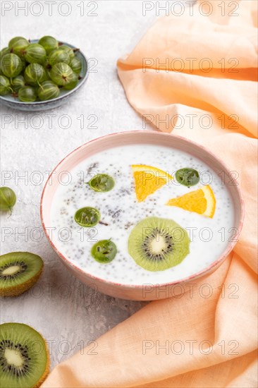 Yogurt with kiwi, gooseberry, chia in ceramic bowl on gray concrete background and orange linen
