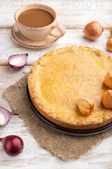 Autumn onion pie and cup of coffee on white wooden background and linen textile. Side view, close