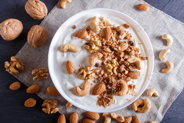 White plate with greek yogurt, granola, almond, cashew, walnuts on black wooden background. top