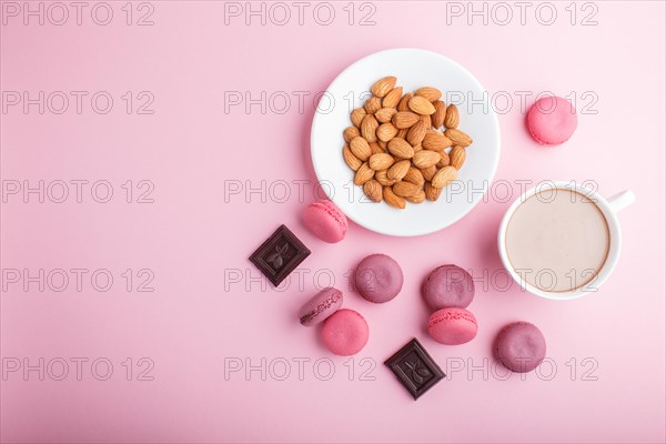 Purple and pink macaron or macaroon cakes with cup of coffee and almonds on pastel pink background.