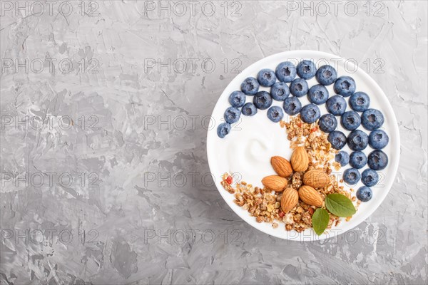 Yoghurt with blueberry, granola and almond in white plate on gray concrete background. top view,