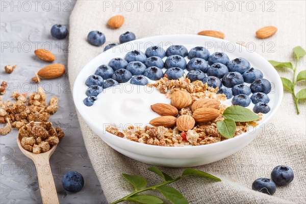 Yoghurt with blueberry, granola and almond in white plate with wooden spoon on gray concrete