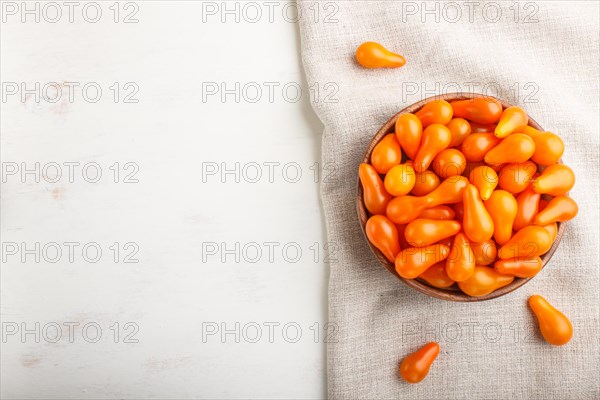 Fresh orange grape tomatoes in wooden bowl on white wooden background with linen napkin. top view,