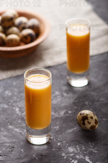Sweet egg liqueur in glass with quail eggs on a black concrete background. Side view, low key,