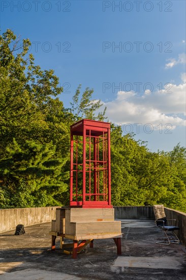 Red wooden telephone booth minus phone and without glass on roof of building on sunny day with blue