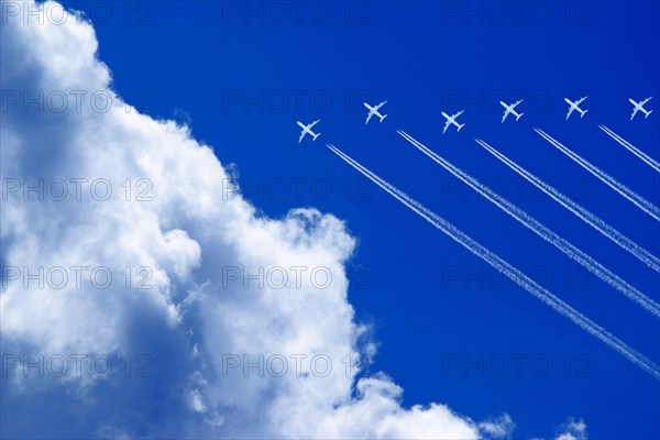 Seven aeroplanes with contrails flying high in the blue sky in formation
