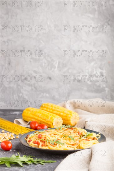 Corn noodles with tomato sauce and arugula on a black concrete background and linen textile. Side