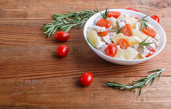 Chicken fillet salad with rosemary, pineapple and cherry tomatoes on brown wooden background. close