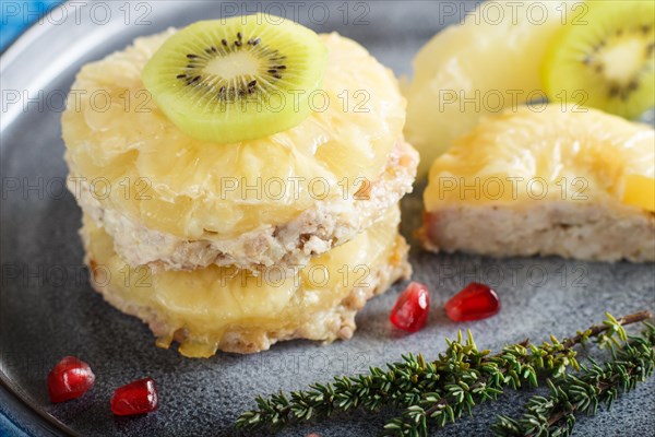 Pieces of baked pork with pineapple, cheese and kiwi on gray plate and blue background, side view,