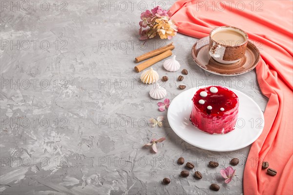 Red cake with souffle cream with cup of coffee on a gray concrete background and red textile. side