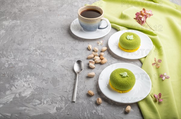 Green mousse cake with pistachio cream and a cup of coffee on a gray concrete background and green