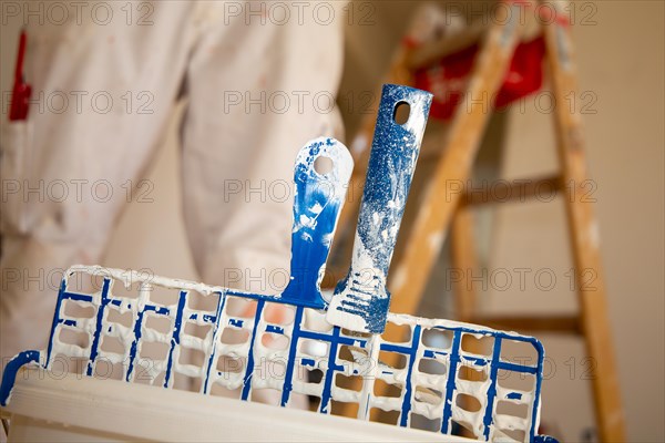 Symbolic image of painting work: Close-up of a paint bucket with scraper grid, in the background a