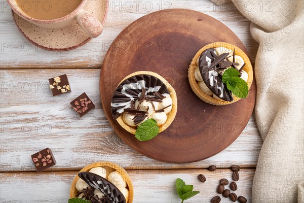 Sweet tartlets with chocolate and cheese cream with cup of coffee on a white wooden background and