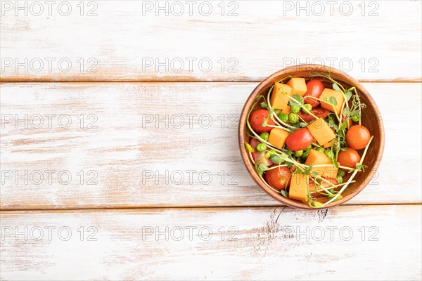 Vegetarian vegetable salad of tomatoes, pumpkin, microgreen pea sprouts on white wooden background.