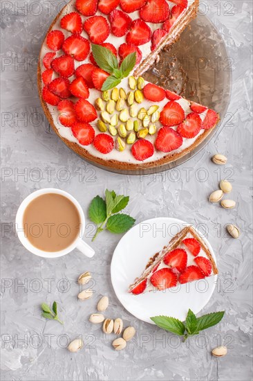 Homemade cake with yoghurt cream, strawberry, pistachio and a cup of coffee on a gray concrete