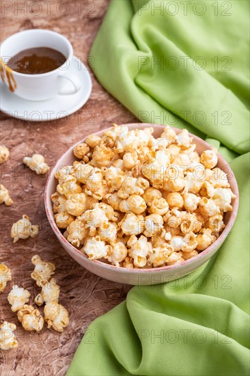 Popcorn with caramel in ceramic bowl on brown concrete background and green textile. Side view,