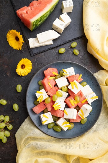 Vegetarian salad with watermelon, feta cheese, and grapes on blue ceramic plate on black concrete