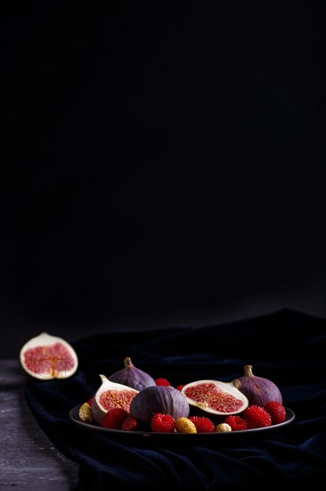 Fresh figs, strawberries and raspberries on blue ceramic plate on black concrete background and