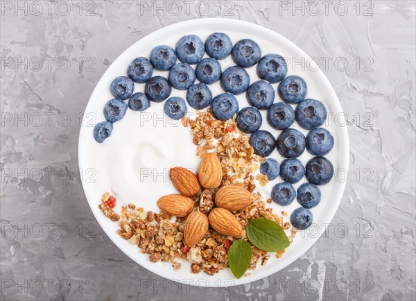 Yoghurt with blueberry, granola and almond in white plate on gray concrete background. top view,