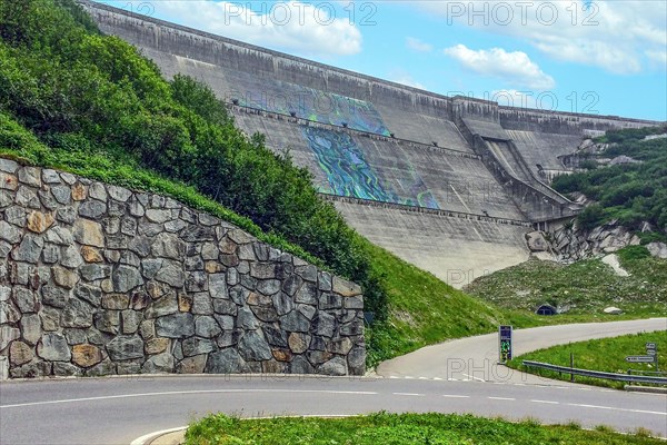 View from road pass road alpine road to road level below in front of outside of large dam wall of