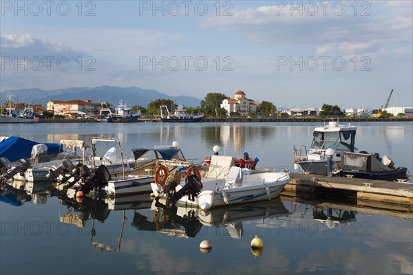 Motorboats are moored at a small jetty in a quiet harbour with a mountain panorama in the