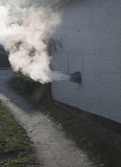 Heat steam emissions from domestic oil powered boiler heating system released through wall of house