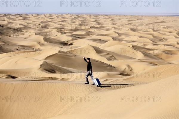 Symbolic image, tourist with suitcase in the desert, Mesr Desert, Iran. The Mesr Desert is part of