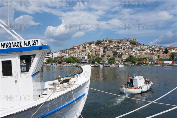 A boat in the foreground with a view of a hillside town by the sea under a partly cloudy sky, Old