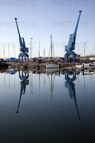 Two large blue industrial cranes reflected in water of Wet Dock marina, Ipswich, Suffolk, England,