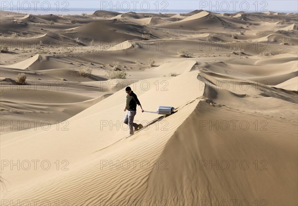 Symbolic image, tourist with suitcase in the desert, Mesr Desert, Iran. The Mesr Desert is part of