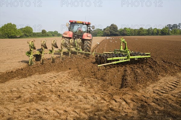 Tractor harrowing soil in field in preparation for planting, Shottisham, Suffolk, England, United
