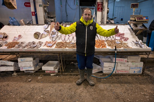 Trader, fishmonger posing proudly in front of his market stall, display of fresh fish and seafood